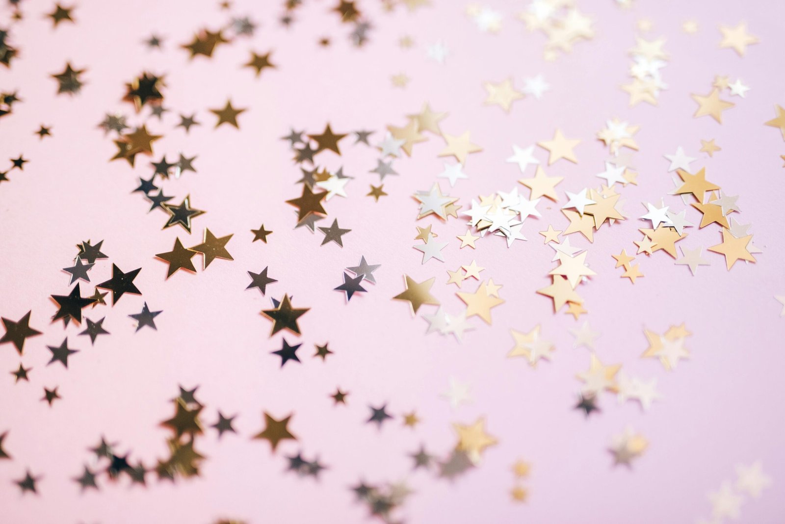 Gold and silver star confetti spread across a pastel pink surface, creating a festive and whimsical effect.