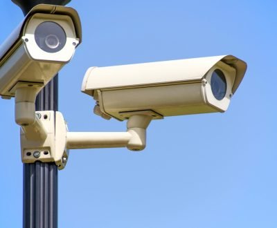 Outdoor security cameras mounted on a pole against a clear blue sky, ensuring vigilant surveillance.